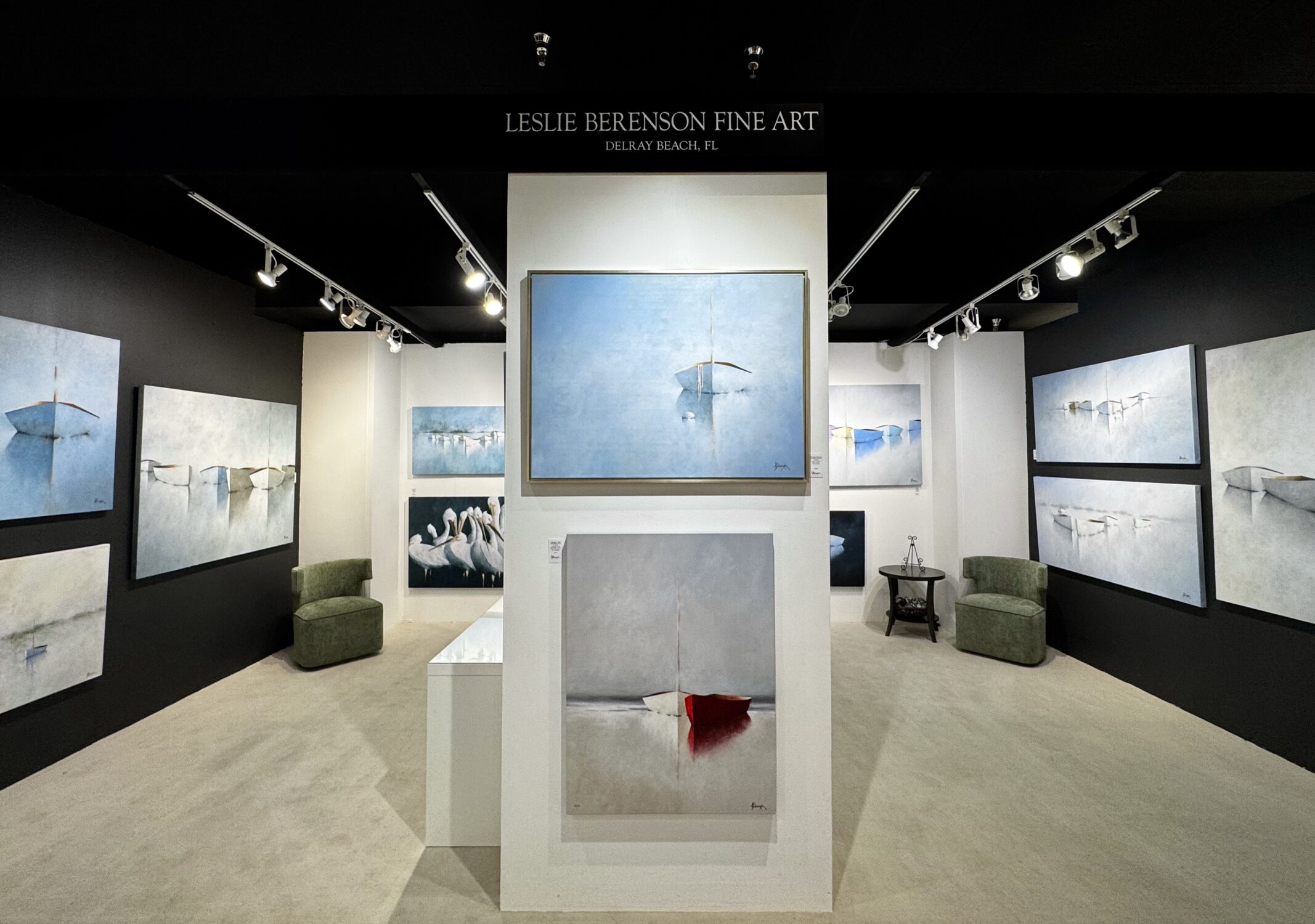 A fine art gallery in serene locations displays minimalist, water-themed paintings with boats and birds in cool blue and white tones. The central artwork features a white boat; below it, a boat with a red accent. Two green armchairs complete the space.